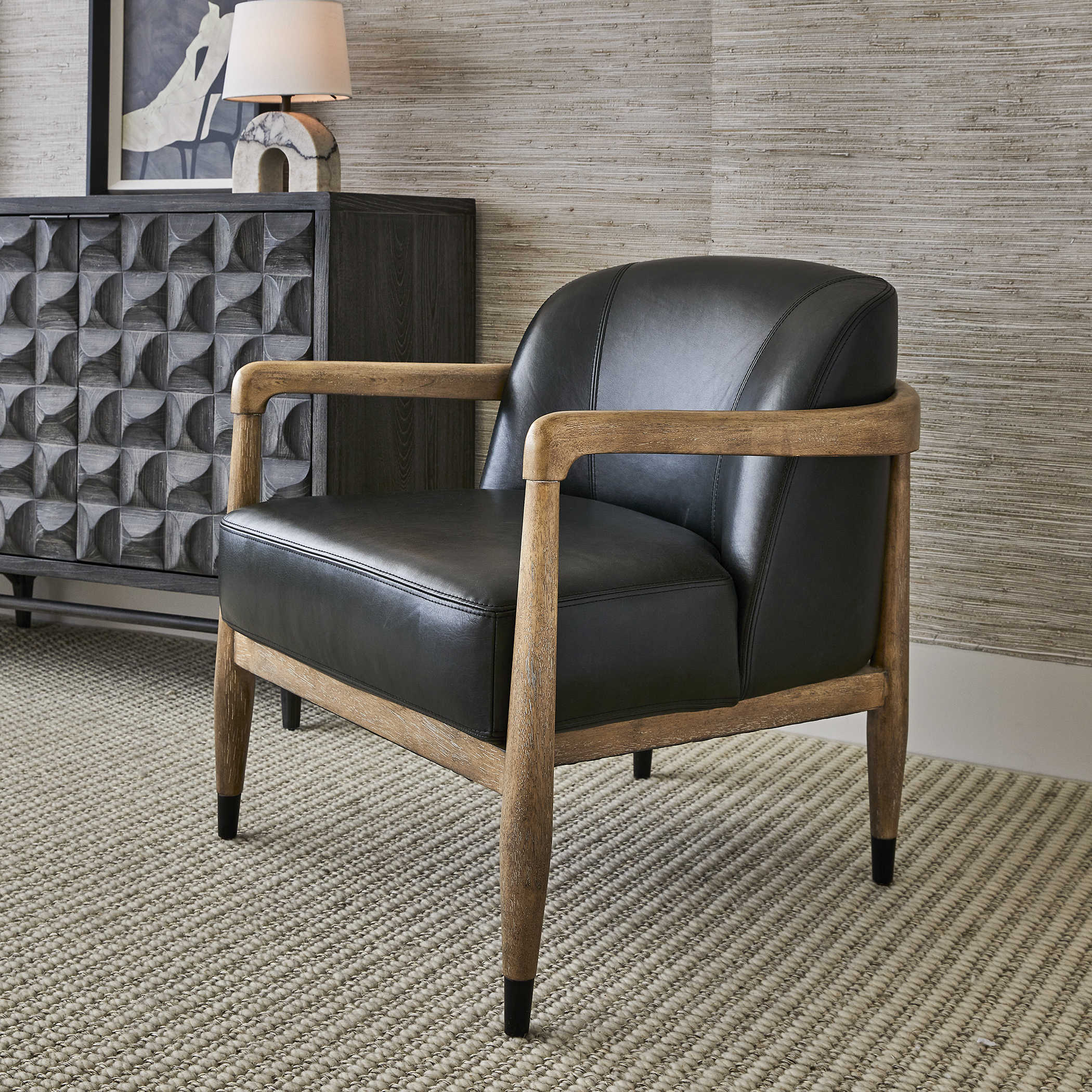Decorate with leather accent chairs. A black leather accent chair with a dark, wooden frame sits in a living room against a textured-wallpapered wall. 