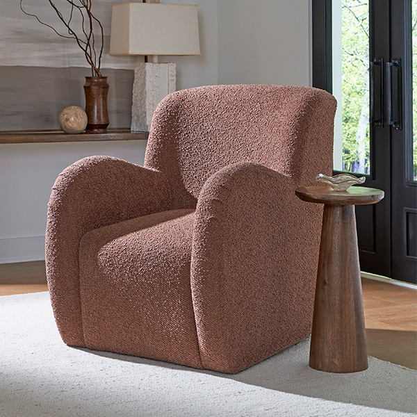 Cozy living space featuring pink decor with a plush dusty rose accent chair, a wooden side table, neutral rug, and stylish modern accents in a well-lit room.