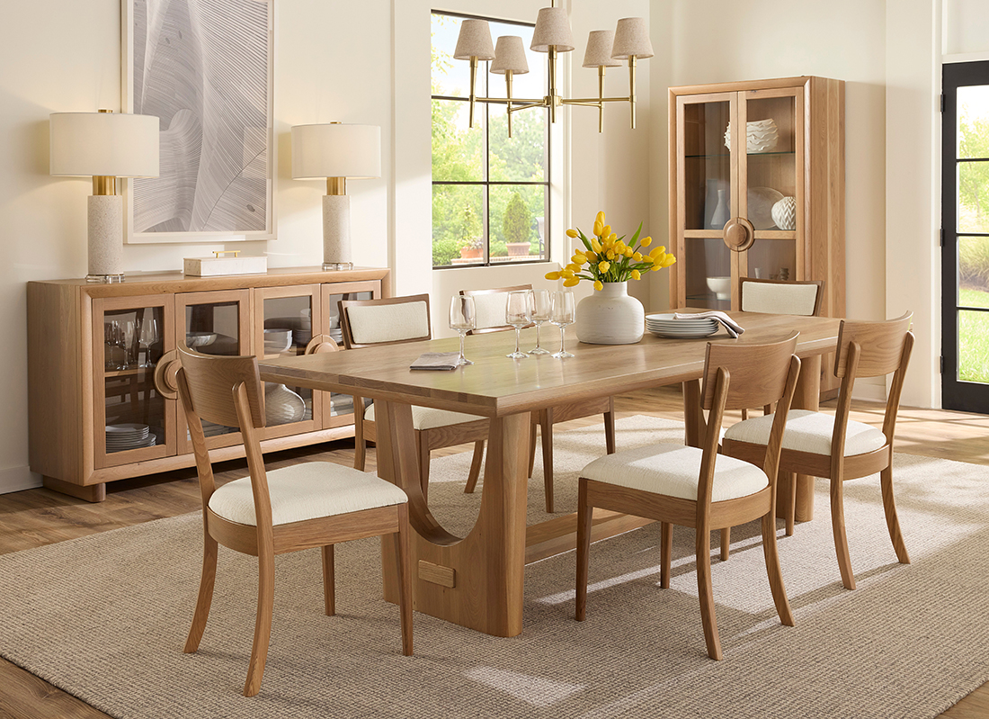 Modern dining room with a sleek wooden table, curved-back chairs, a stylish sideboard, and elegant lighting in a bright, neutral-toned space.