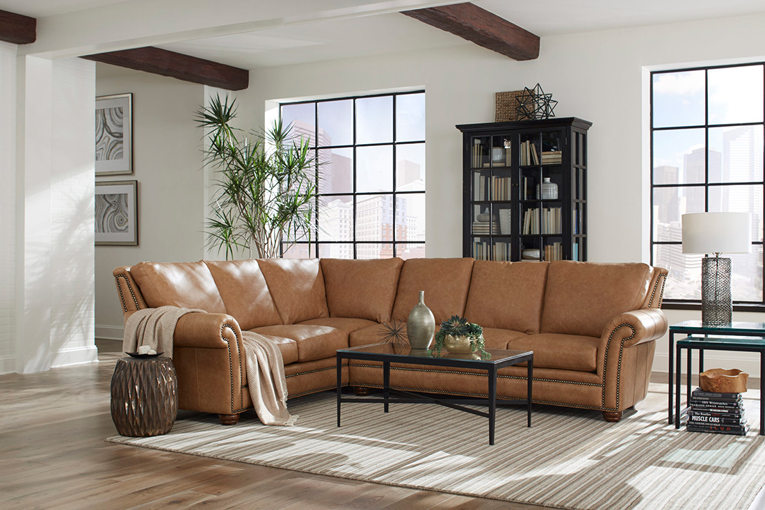 Spacious living room featuring a tan leather sofa sectional with nailhead trim, large windows, and modern industrial decor elements.
