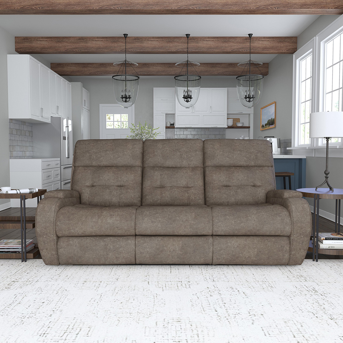 Modern farmhouse living space with a taupe leather sofa recliner, exposed wood ceiling beams, and a bright white kitchen in the background.