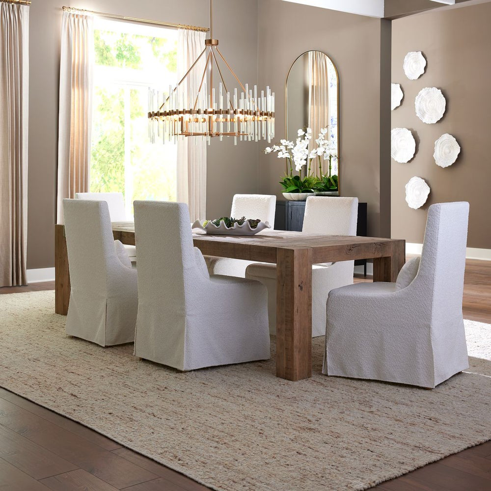 Modern dining room featuring classic furniture touches, with a rustic wood table, slipcovered chairs, and a statement chandelier.