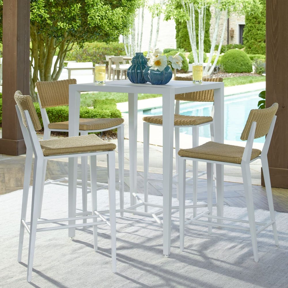 Stylish outdoor furniture from Uttermost featuring a white bar-height dining table and woven bar stools by a poolside patio.