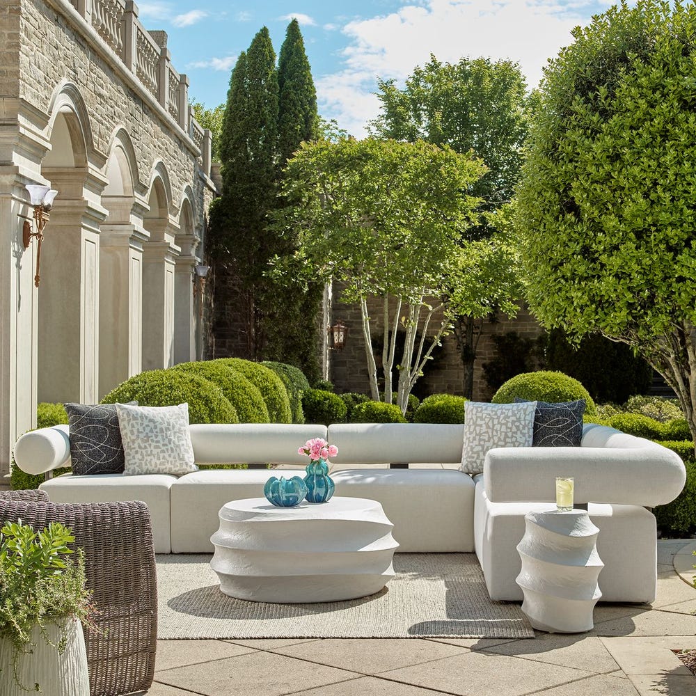 Stylish outdoor furniture from Uttermost featuring a modern white sectional sofa and sculptural tables in a luxury garden setting.