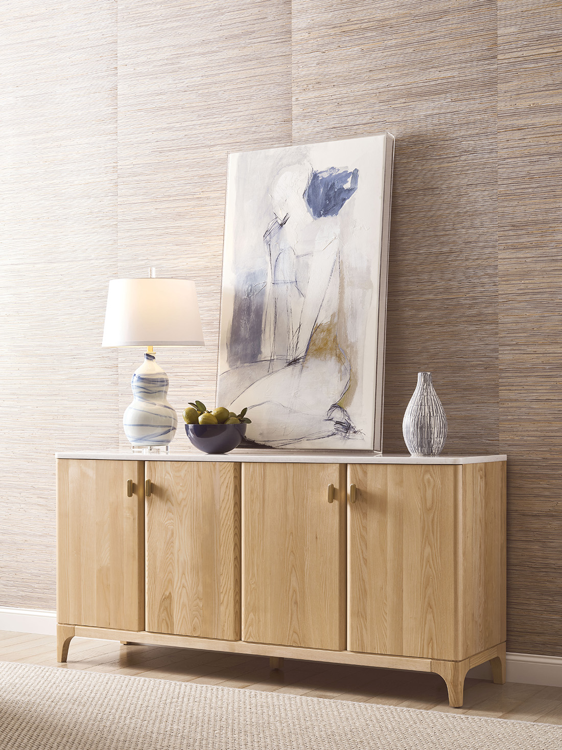 Modern wood furniture credenza with a light ash finish, topped with marble, abstract art, and decorative accessories in a contemporary room setting.